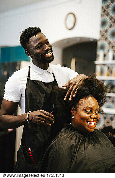 Smiling male barber cutting hair of female customer in salon