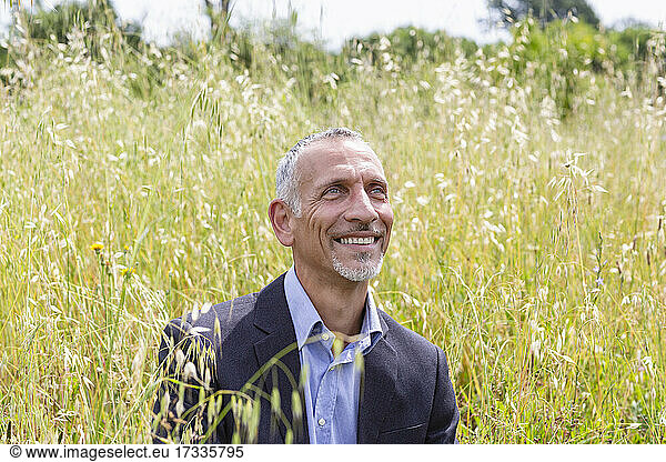 Smiling male business professional looking away while sitting in grassy field
