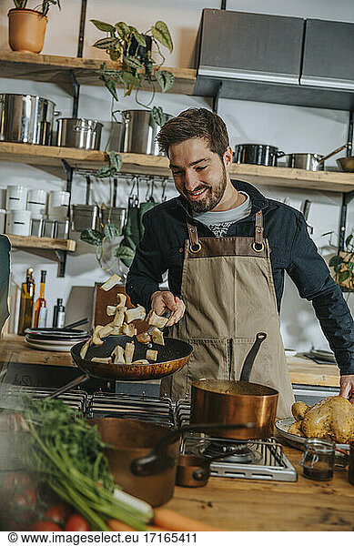 Smiling male chef tossing mushroom in frying pan while standing in kitchen