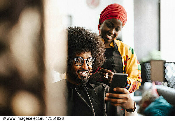Smiling male customer taking selfie with female barber at hair salon