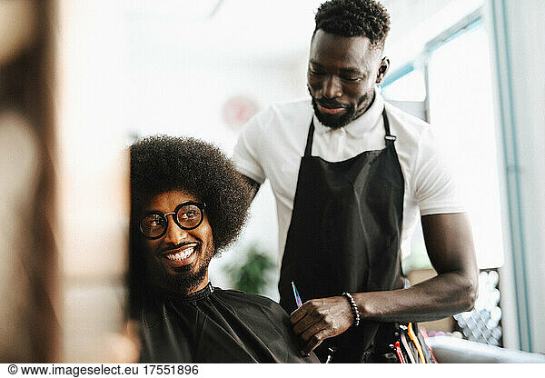 Smiling male customer talking with barber in hair salon
