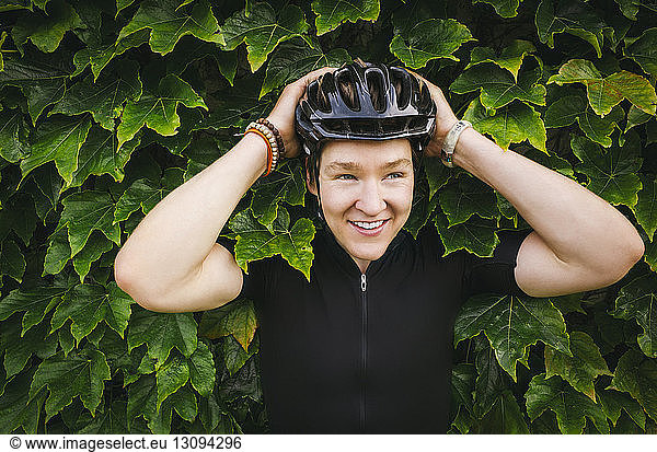 Smiling male cyclist wearing helmet against ivy