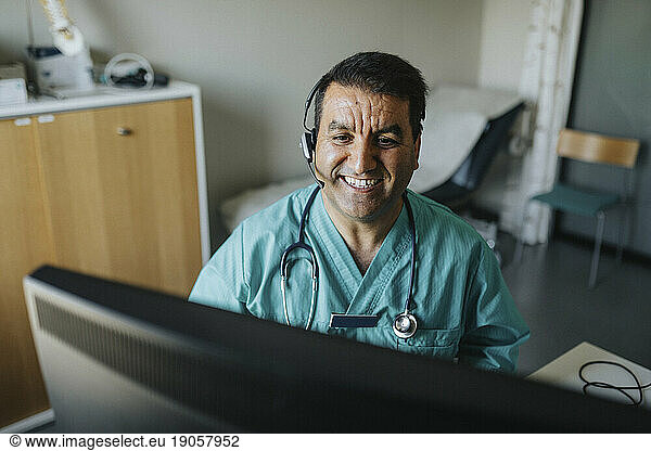 Smiling male doctor wearing headset giving advice through video call in hospital