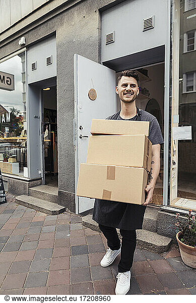 Smiling male entrepreneur carrying boxes while standing outside store