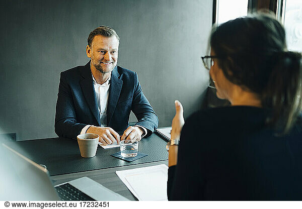 Smiling male entrepreneur listening to female colleague at conference table in board room