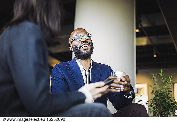 Smiling male entrepreneur looking away while sitting with female coworker in office