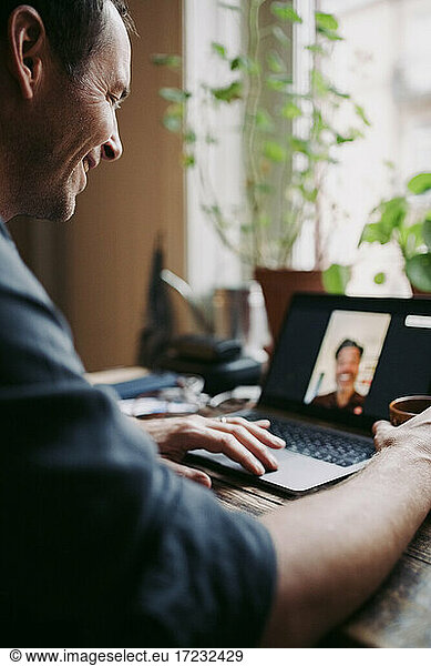 Smiling male entrepreneur on video call discussing with colleague at home during COVID-19