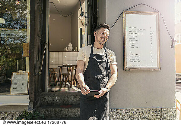 Smiling male entrepreneur with digital tablet outside cafe
