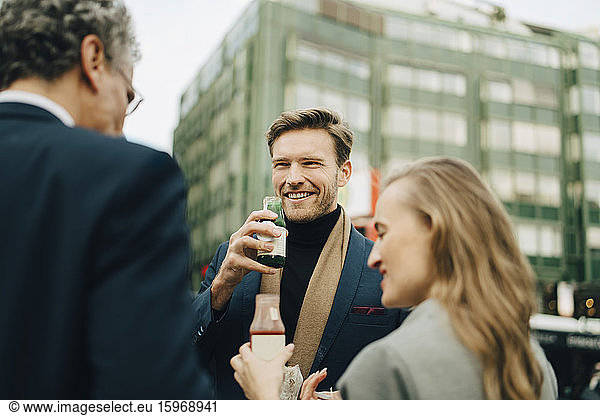 Smiling male entrepreneur with drink looking at coworkers in city