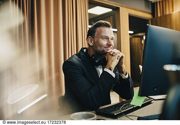 Smiling male entrepreneur with hand on chin working over laptop in office