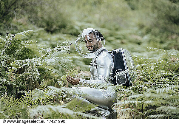 Smiling male environmentalist with protective suit examining plants in forest