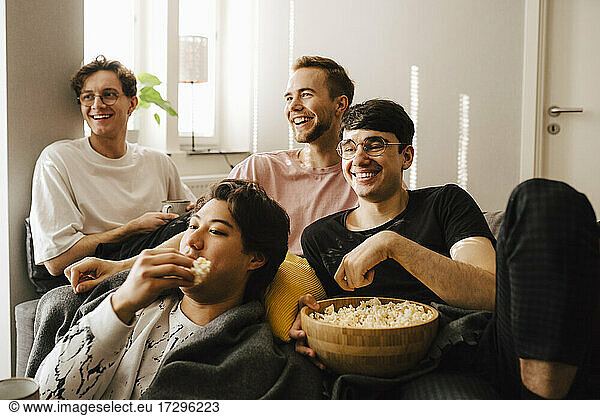 Smiling male friends eating popcorn while watching sports at home