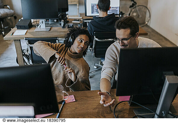 Smiling male hacker discussing with female colleague at desk in creative office