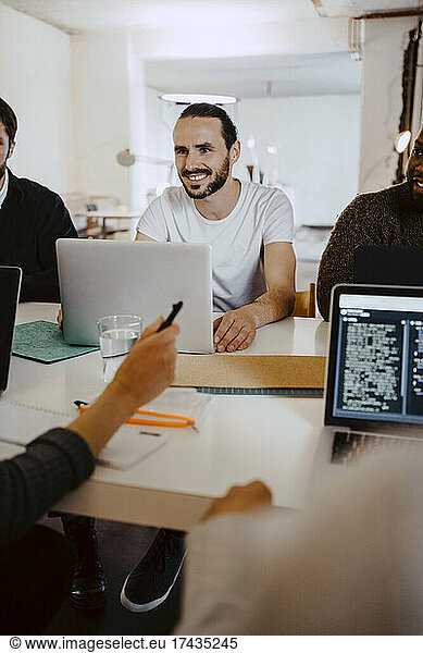 Smiling male hacker in business meeting with colleagues at creative office