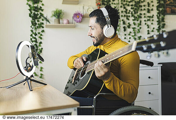 Smiling male influencer playing guitar on wheelchair