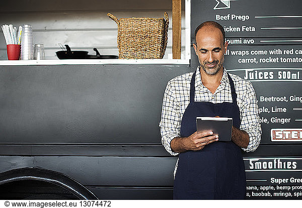 Smiling male owner using tablet computer while standing against food truck