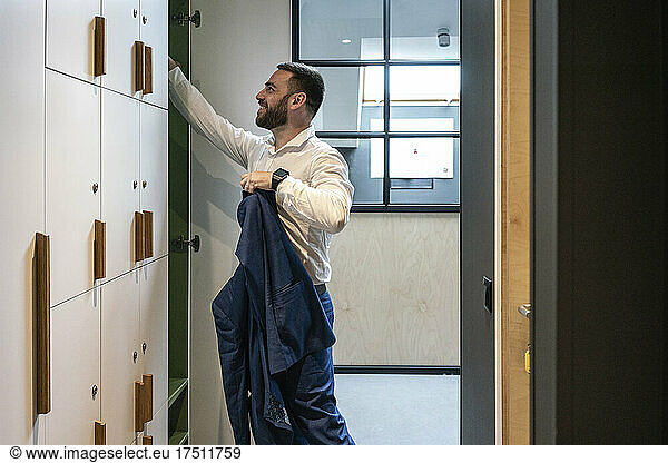 Smiling male professional holding suit while searching in locker