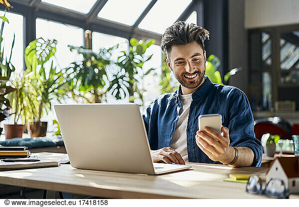 Smiling male professional using mobile phone while sitting at desk in office