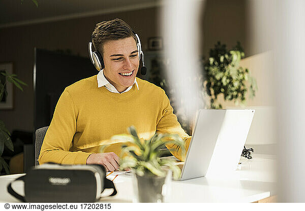 Smiling male professional wearing headphones attending business meeting in home office