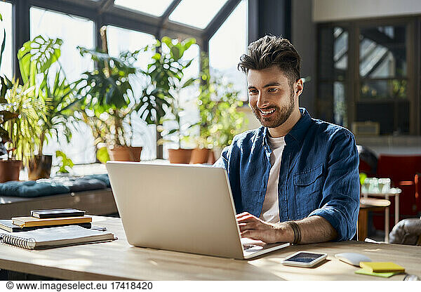 Smiling male professional working on laptop at desk in office