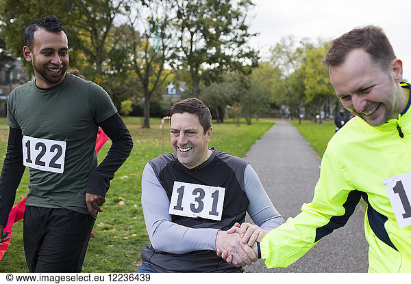 Smiling male runner shaking hands with friend in wheelchair at charity race in park