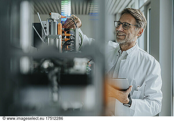 Smiling male scientist holding digital tablet inventing machinery in laboratory