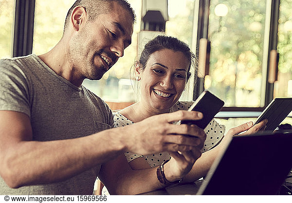 Smiling male showing smart phone to female partner in cafe