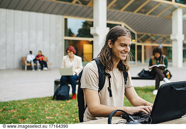 Smiling male student e-learning through laptop in campus