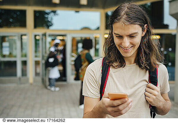 Smiling male student using mobile phone in university