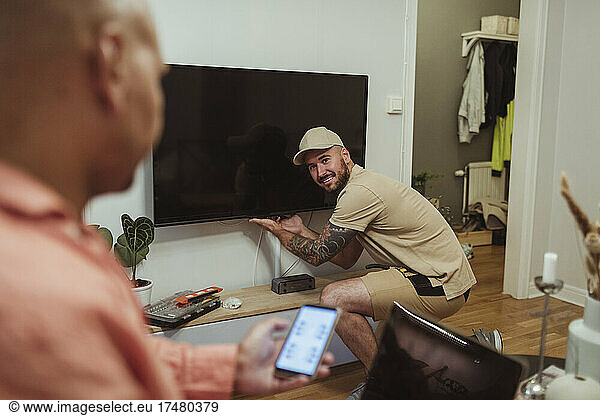Smiling male technician looking at mature man using smart phone in living room