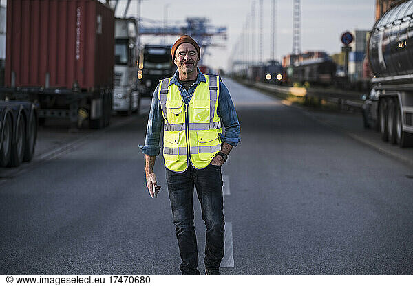 Smiling male truck driver with hand in pocket walking on street at dock