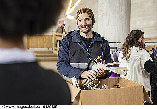 Smiling male worker unpacking hangers from cardboard box at recycling center