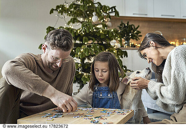 Smiling man and daughter joining puzzle by woman with dog at home