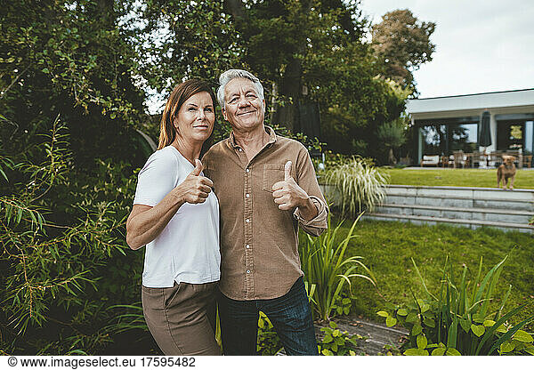 Smiling man and woman gesturing thumbs up at backyard