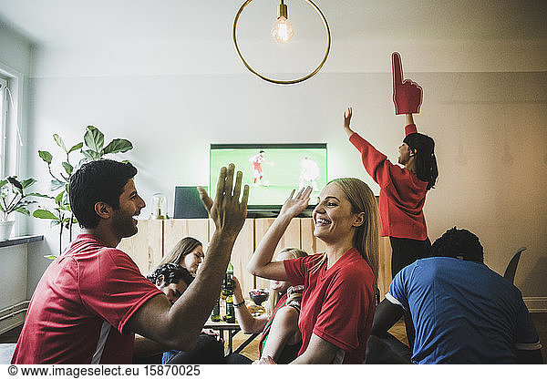 Smiling man and woman high-fiving while celebrating victory with friends at home