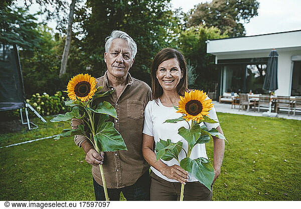 Smiling man and woman holding sunflowers in garden