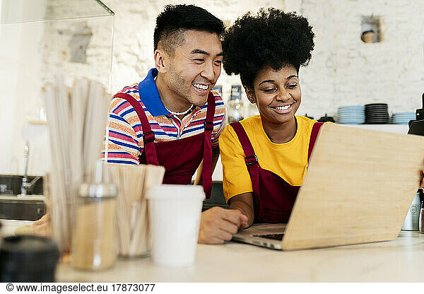 Smiling man and woman sharing laptop in coffee shop
