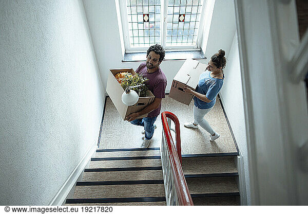 Smiling man and woman with cardboard boxes moving up on staircase