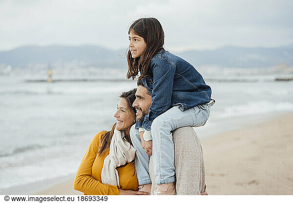 Smiling man and woman with daughter standing together at beach