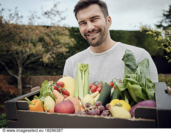 Smiling man carrying a fresh vegetable box in garden