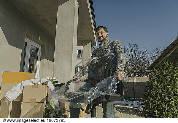 Smiling man carrying wrapped chair into new house
