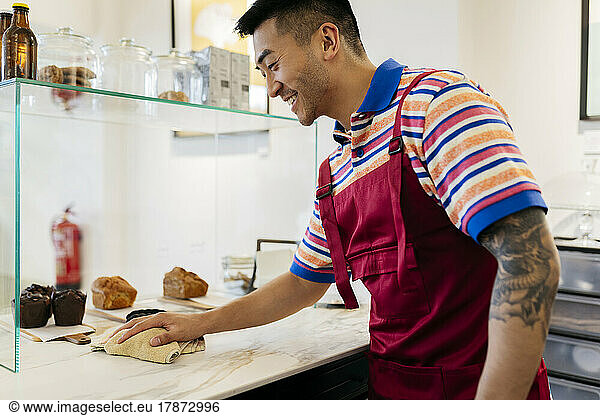 Smiling man cleaning counter with rag in coffee shop
