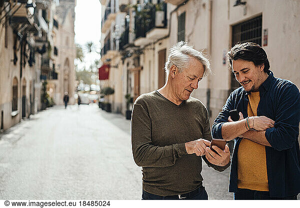 Smiling man discussing with father over smart phone on street