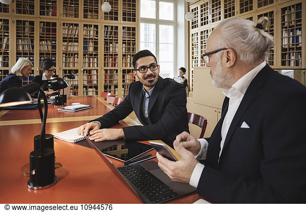 Smiling man discussing with senior lawyer at table in library