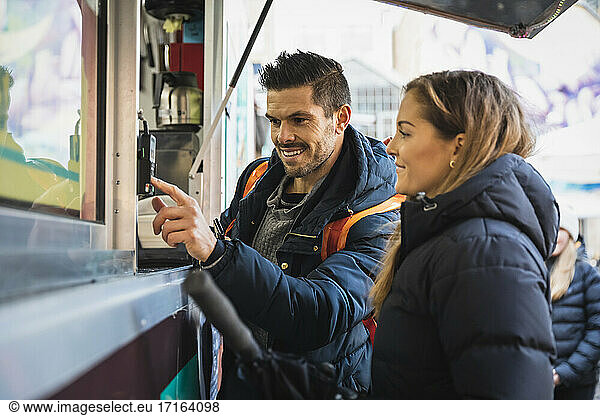 Smiling man doing contactless payment standing by woman at food truck