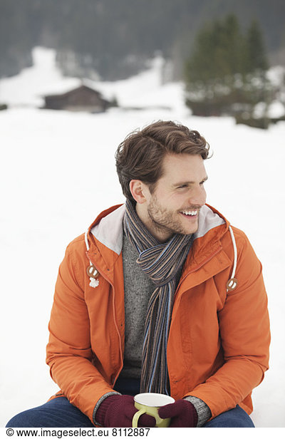 Smiling man drinking coffee in snowy field