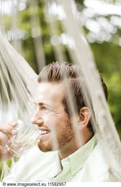Smiling man drinking while resting in hammock