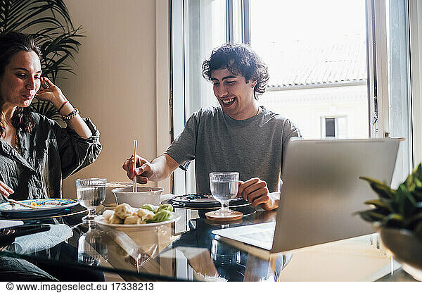 Smiling man eating food while sitting by woman at home