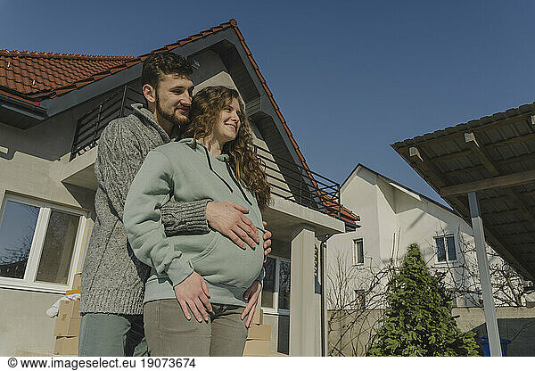 Smiling man embracing pregnant woman outside house