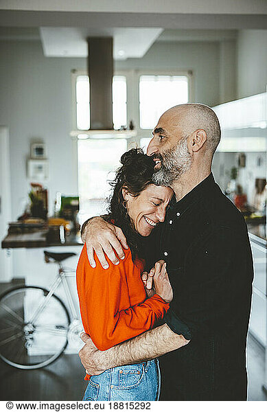 Smiling man embracing woman standing at home